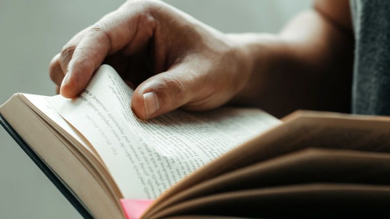 Das Bild zeigt ein aufgeschlagenes Buch, das durch eine Person gehalten wird.