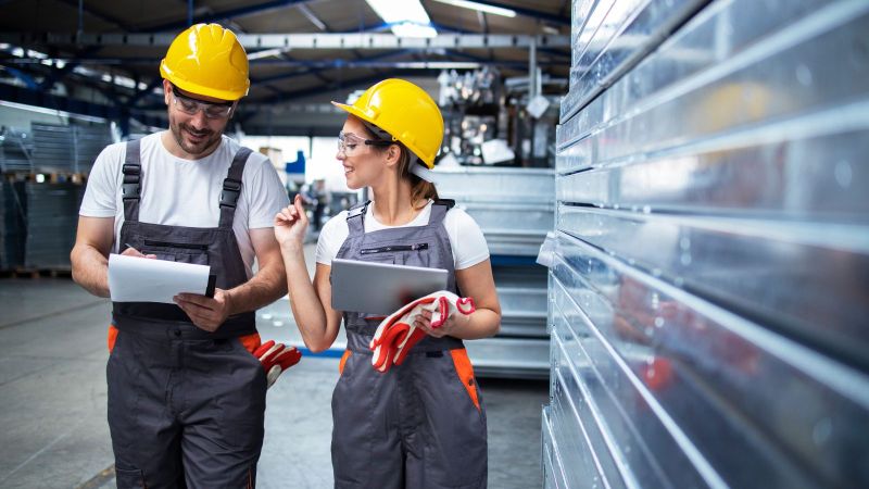 Das Bild zeigt arbeitende Fabrikarbeiter mit Helm im Gespräch