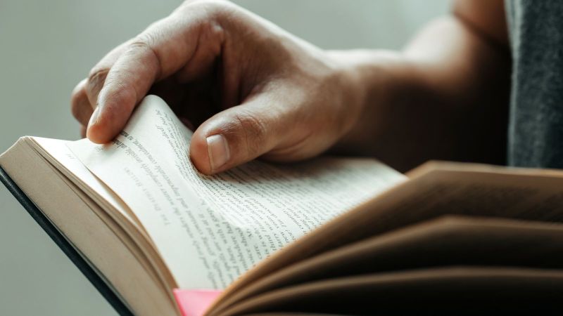 Das Bild zeigt ein aufgeschlagenes Buch, das durch eine Person gehalten wird.