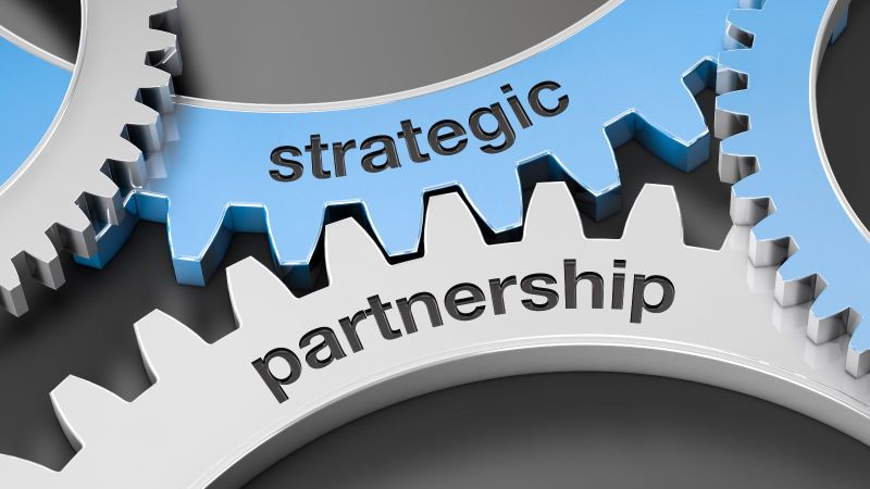 Vier Zahnräder, die aufeinander gestapelt sind, wobei zwei davon blau eingefärbt sind. Auf zwei der Zahnräder stehen die Worte „strategic“ und „partnership“.