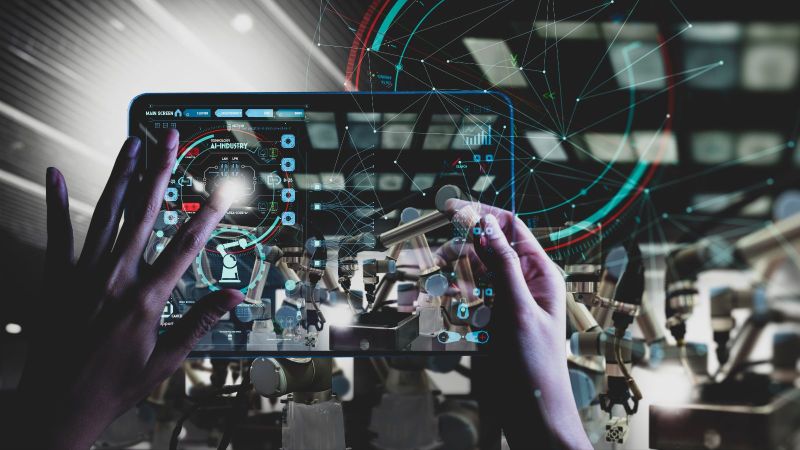 Das Bild zeigt Hände, die per holographischem Bildschirm die Funktion von Industrierobotern überwachen. 
