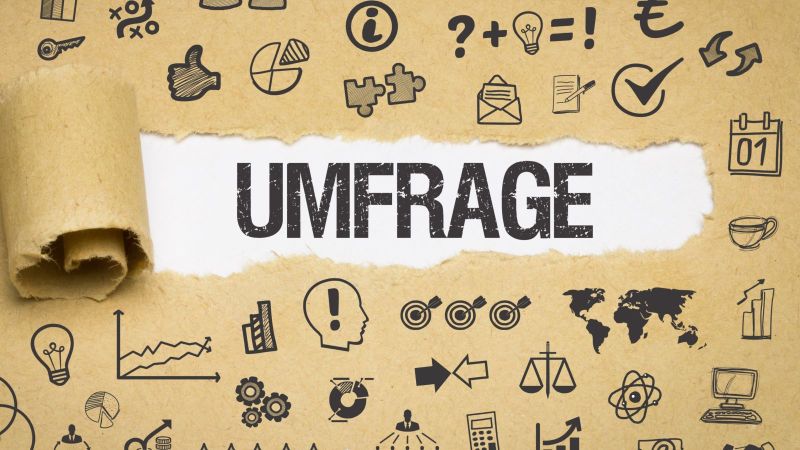 Das Bild zeigt Papier, auf dem sich verschiedenste Symbole befinden. In der Mitte des Bildes ist das Papier aufgerissen und das Wort „Umfrage“ ist zu lesen.