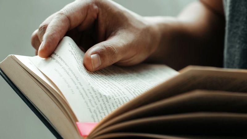 Das Bild zeigt ein aufgeschlagenes Buch, das durch eine Person gehalten wird.