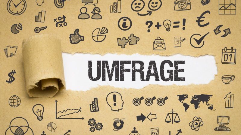 Das Bild zeigt Papier, auf dem sich verschiedenste Symbole befinden. In der Mitte des Bildes ist das Papier aufgerissen und das Wort „Umfrage“ ist zu lesen.