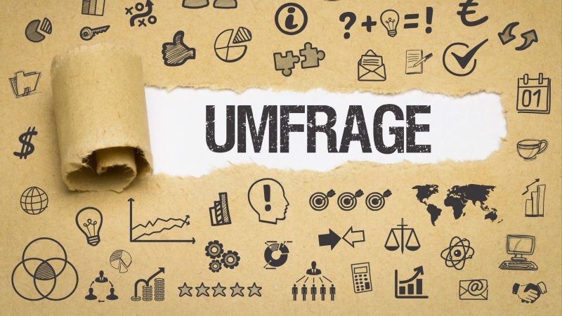 Das Bild zeigt Papier, auf dem sich verschiedenste Symbole befinden. In der Mitte des Bildes ist das Papier aufgerissen und das Wort „Umfrage“ ist zu lesen.