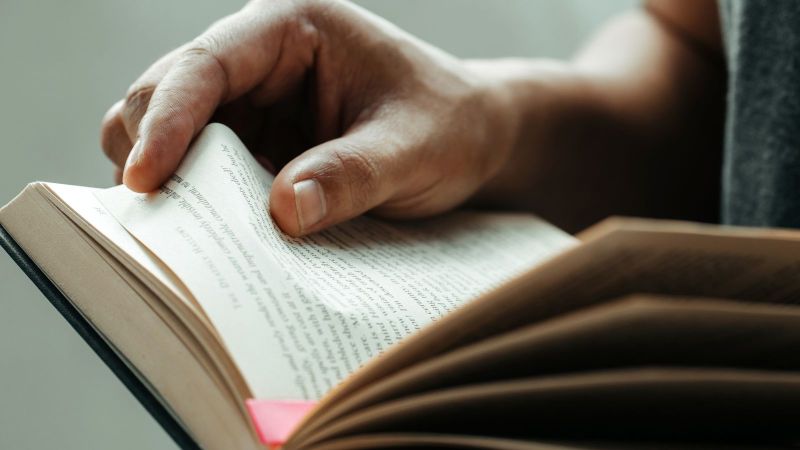 Das Bild zeigt ein aufgeschlagenes Buch, das durch eine Person gehalten wird.