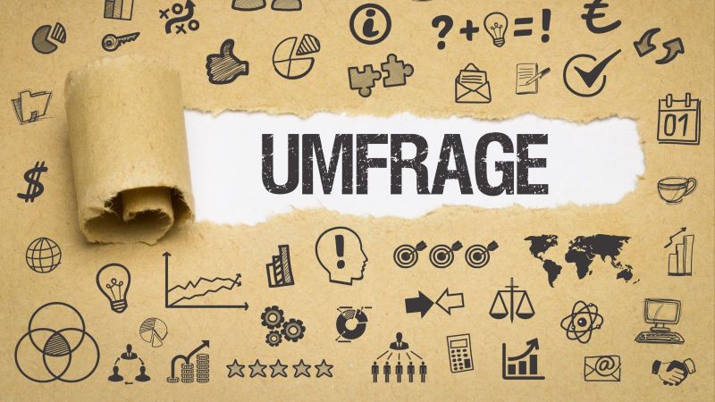 Das Bild zeigt Papier, auf dem sich verschiedenste Symbole befinden. In der Mitte des Bildes ist das Papier aufgerissen und das Wort „Umfrage“ ist zu lesen.