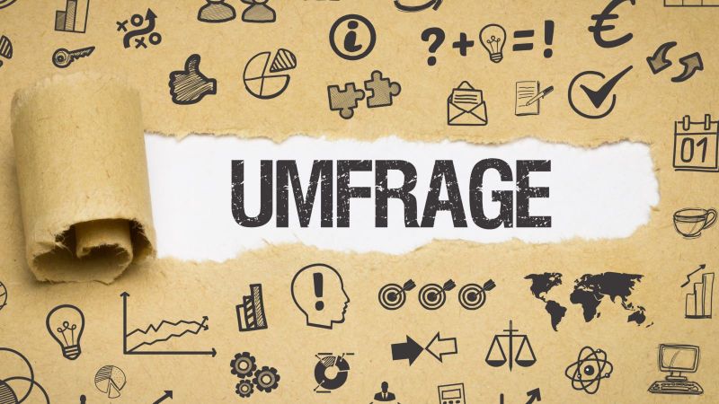 Das Bild zeigt Papier, auf dem sich verschiedenste Symbole befinden. In der Mitte des Bildes ist das Papier aufgerissen und das Wort „Umfrage“ ist zu lesen.