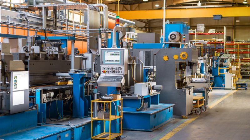 Dieses Bild zeigt eine Fabrikhalle, in der eine große Produktionsanlage für die Metallverarbeitung betriebsbereit steht. Im Zentrum des Bildes befindet sich das Steuerpult der Anlage.