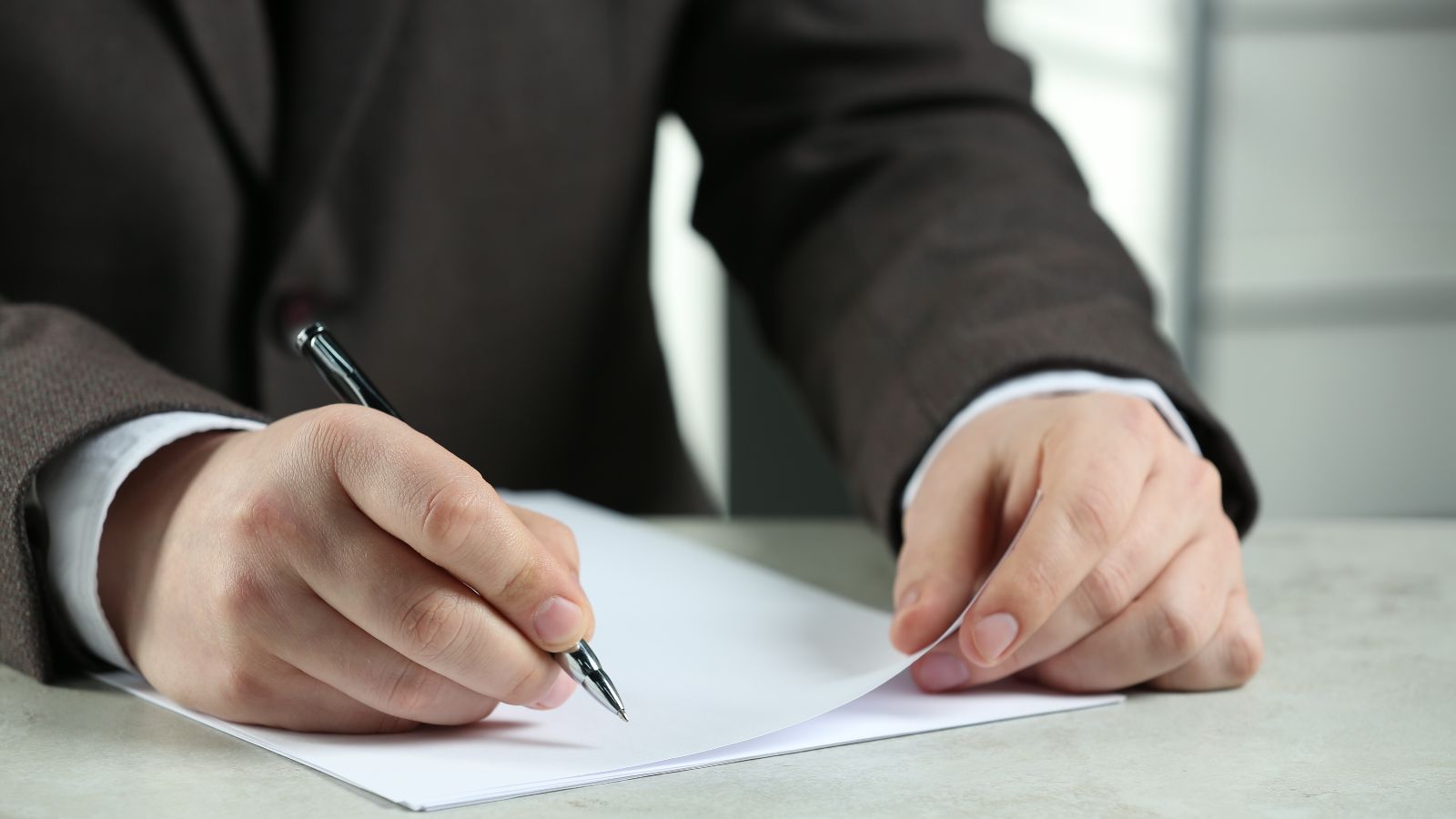 Das Bild zeigt einen Mann im Anzug, der auf ein Stück Papier schreibt. 