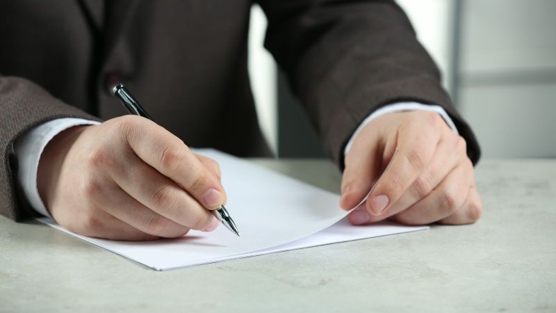 Das Bild zeigt eine Hand, die einen Stift hält über mehreren Blättern Papier.