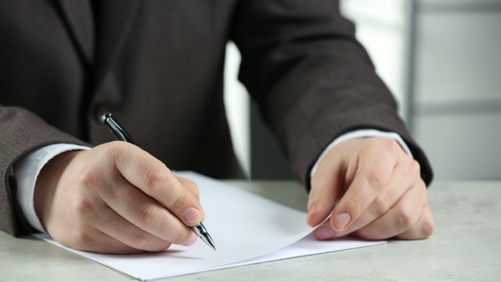 Das Bild zeigt einen Mann im Anzug, der auf ein Stück Papier schreibt.
