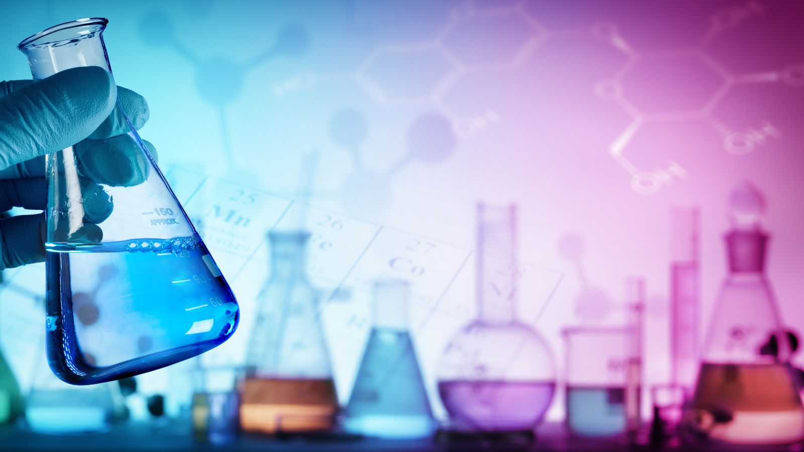 Das Bild zeigt eine Hand, die einen Glaskolben mit einer blauen Flüssigkeit hält. Im Hintergrund sind weitere Glasbehälter mir verschiedenfarbigen Flüssigkeiten zu sehen.