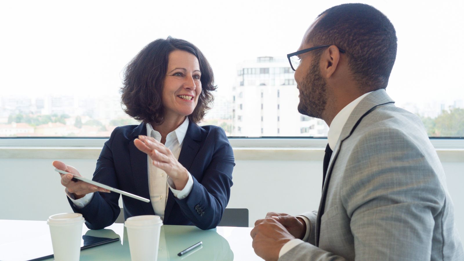 Das Bild zeigt zwei Menschen im Anzug, die sich anlächeln, während sie etwas besprechen.